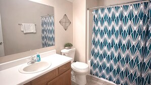 A bathroom with a white sink, wooden vanity, a toilet, a shower curtain with a geometric pattern, and a mirror with a towel hanging on the wall. - Federal Ct- Charming 3-bedroom near Ag Center and MTSU in Murfreesboro (Murfreesboro)