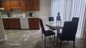 A dining area with a round table and four chairs, a kitchen with wooden cabinets, a dishwasher, and a ceiling light fixture. - Federal Ct- Charming 3-bedroom near Ag Center and MTSU in Murfreesboro (Murfreesboro)