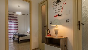 Ein Schlafzimmer mit einem Bett, einem Nachttisch mit Lampe, einer Wand mit dekorativem Zitat und einer Tür zu einem anderen Raum.