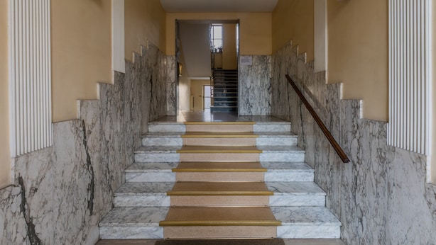 Eine Marmortreppe mit Handlauf, die zu einer Tür oben führt.