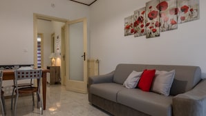 Ein Wohnzimmer mit grauem Sofa, einem Esstisch mit Stühlen und einer Tür zu einem anderen Raum.