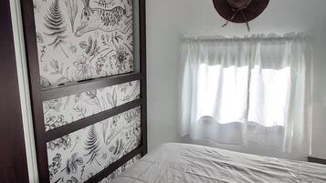 Ein Schlafzimmer mit einem Bett, einem Fenster mit Vorhängen, einer Wand mit Blumenmuster und einem Deckenventil.