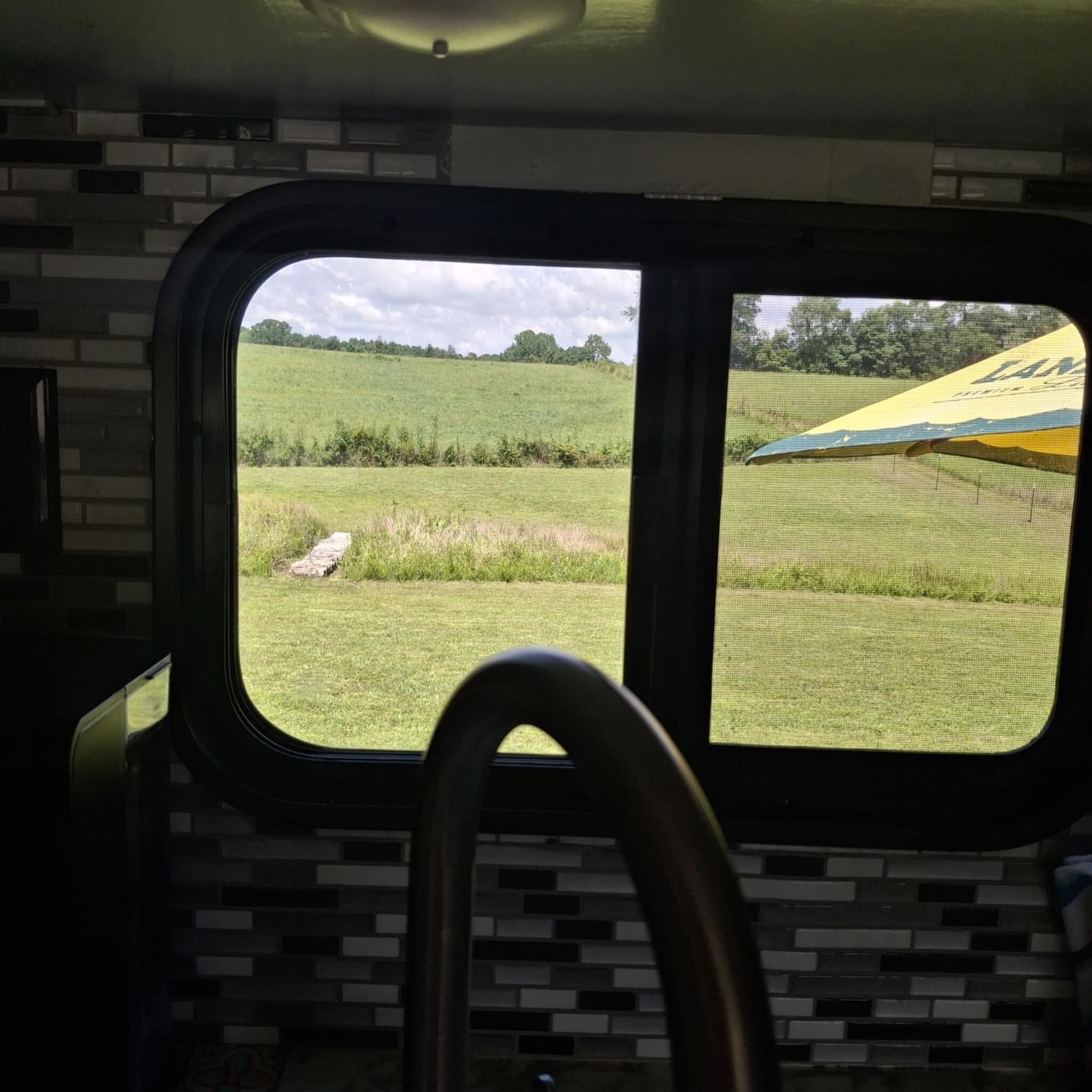 A vehicle interior with a window view of a grassy field and a yellow tent.
