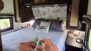 A bedroom with a bed, pillows, a bedside table, a window, and a headboard with a floral pattern.