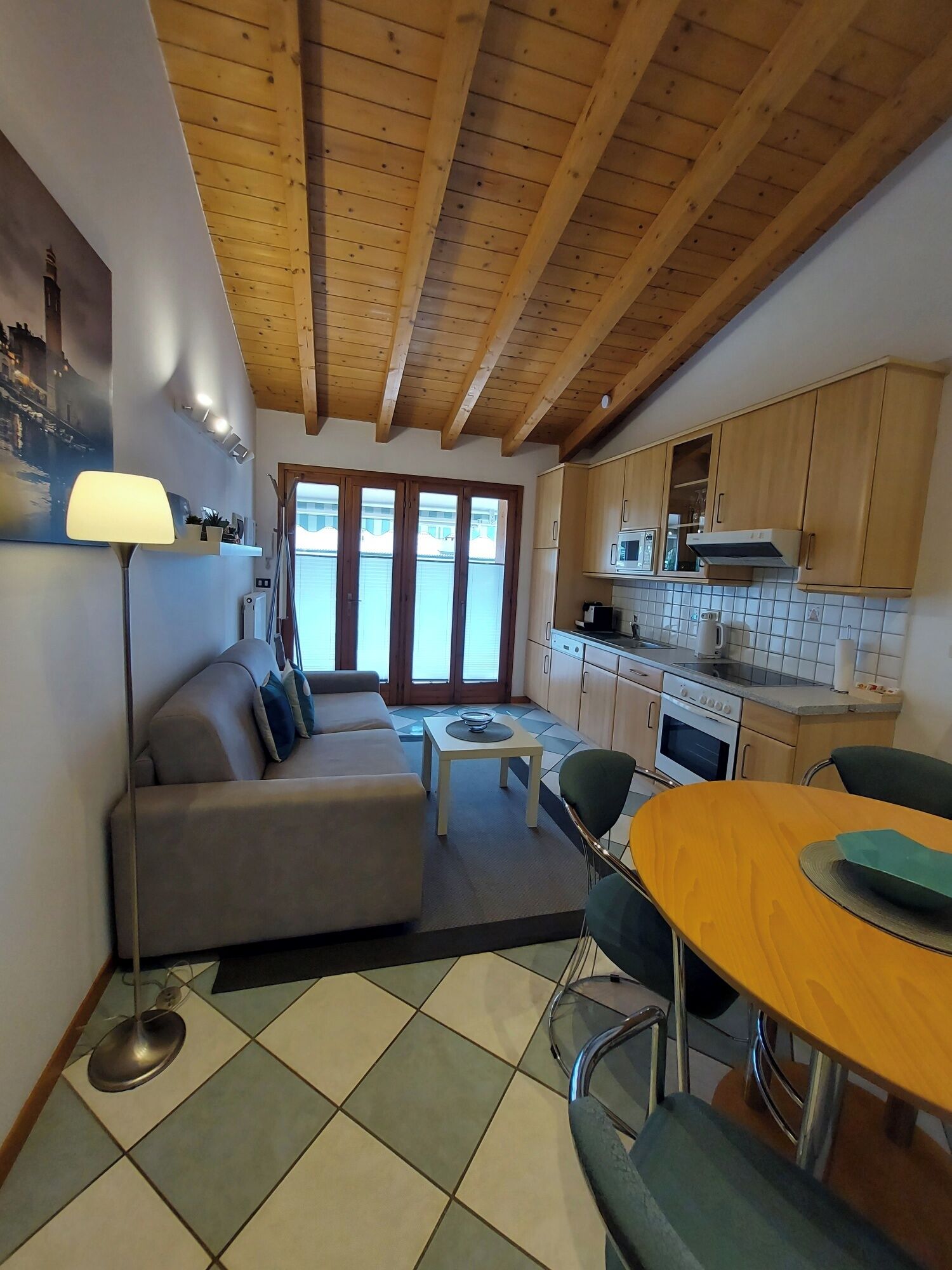 Un espacio habitable compacto con techo de madera, un sofá, una mesa de comedor con sillas, una zona de cocina y un ventanal grande.