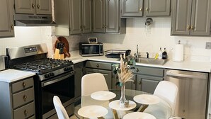 Una cocina moderna con armarios grises, estufa de acero inoxidable y una mesa de comedor de vidrio con sillas blancas.
