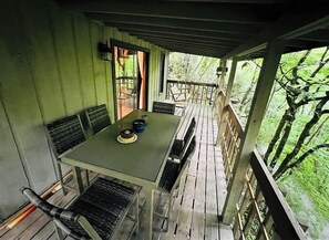 A covered outdoor dining area with a table and chairs, surrounded by a wooden deck and a view of the forest. - * Plentiful Porches * Hot Tub * King Bed * Views * (Watauga County)