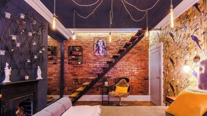 Une pièce avec un mur en briques, un escalier, une cheminée et un lit agrémenté d’un coussin décoratif blanc et jaune.