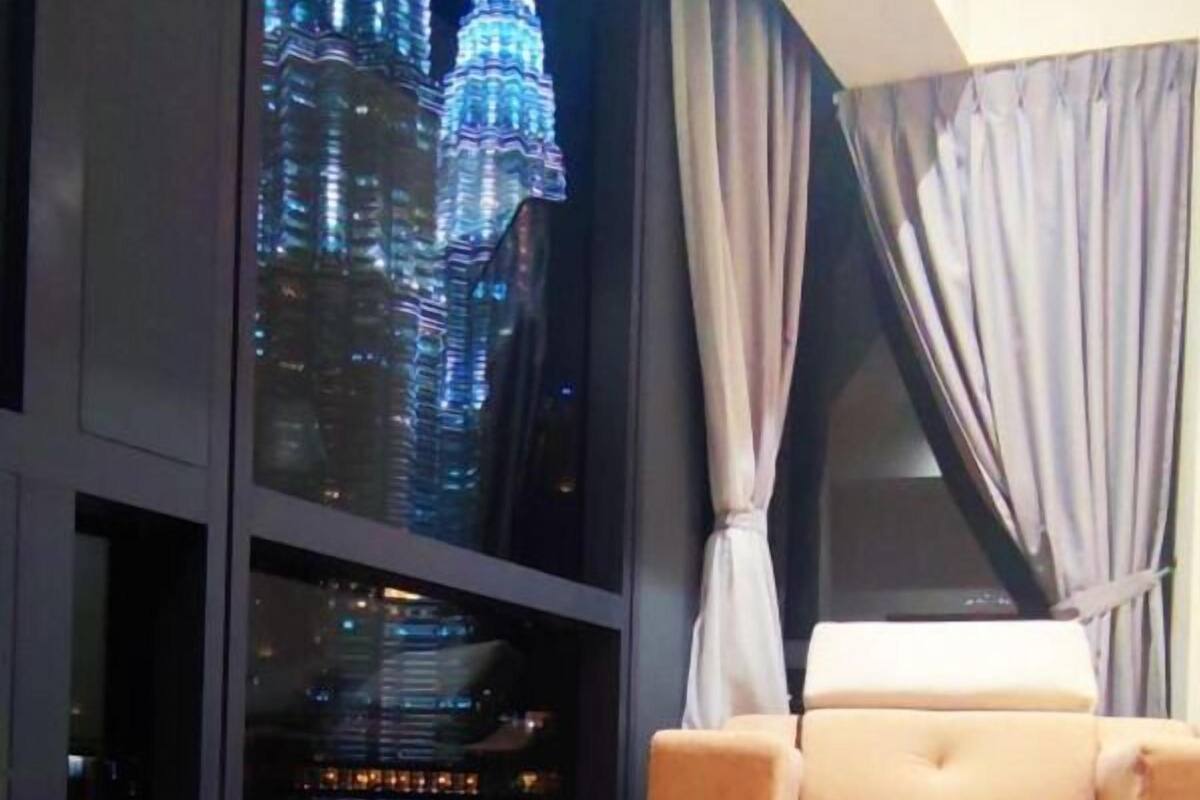 Une chambre avec une grande fenêtre donnant sur les tours Petronas la nuit.