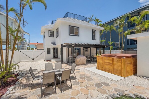 A two-story house with a patio area featuring a table and chairs, a hot tub, and a covered seating area. - BIG 4/4: OCEAN VIEW+ROOFTOP DECK+ SWIMSPA+POOL TABLE+PUTTING GREEN-SLEEPS 13!!! (Bradenton Beach)