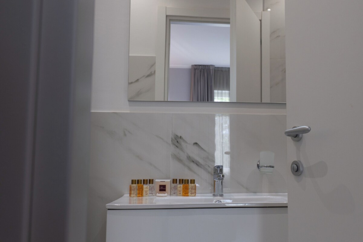 Un baño con lavamanos de mármol, un espejo y una puerta de ducha.