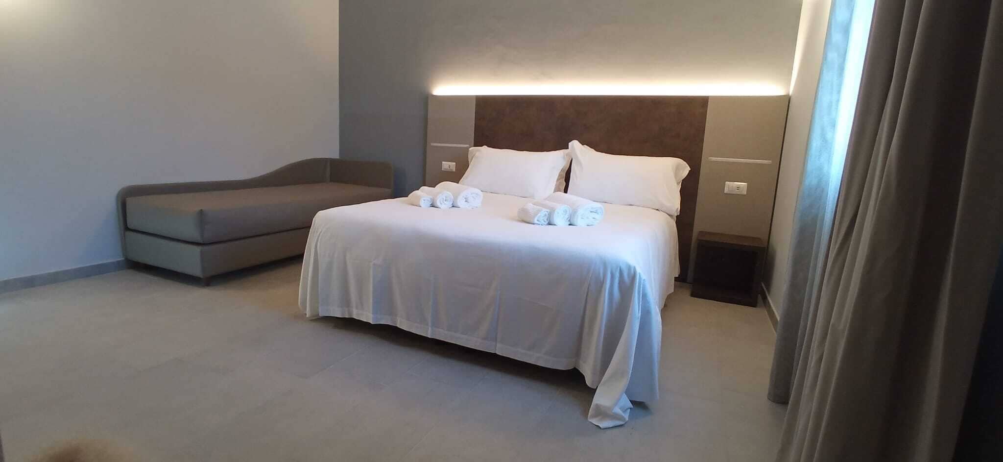 A modern hotel room with a large bed, a bedside table, and a built-in headboard.