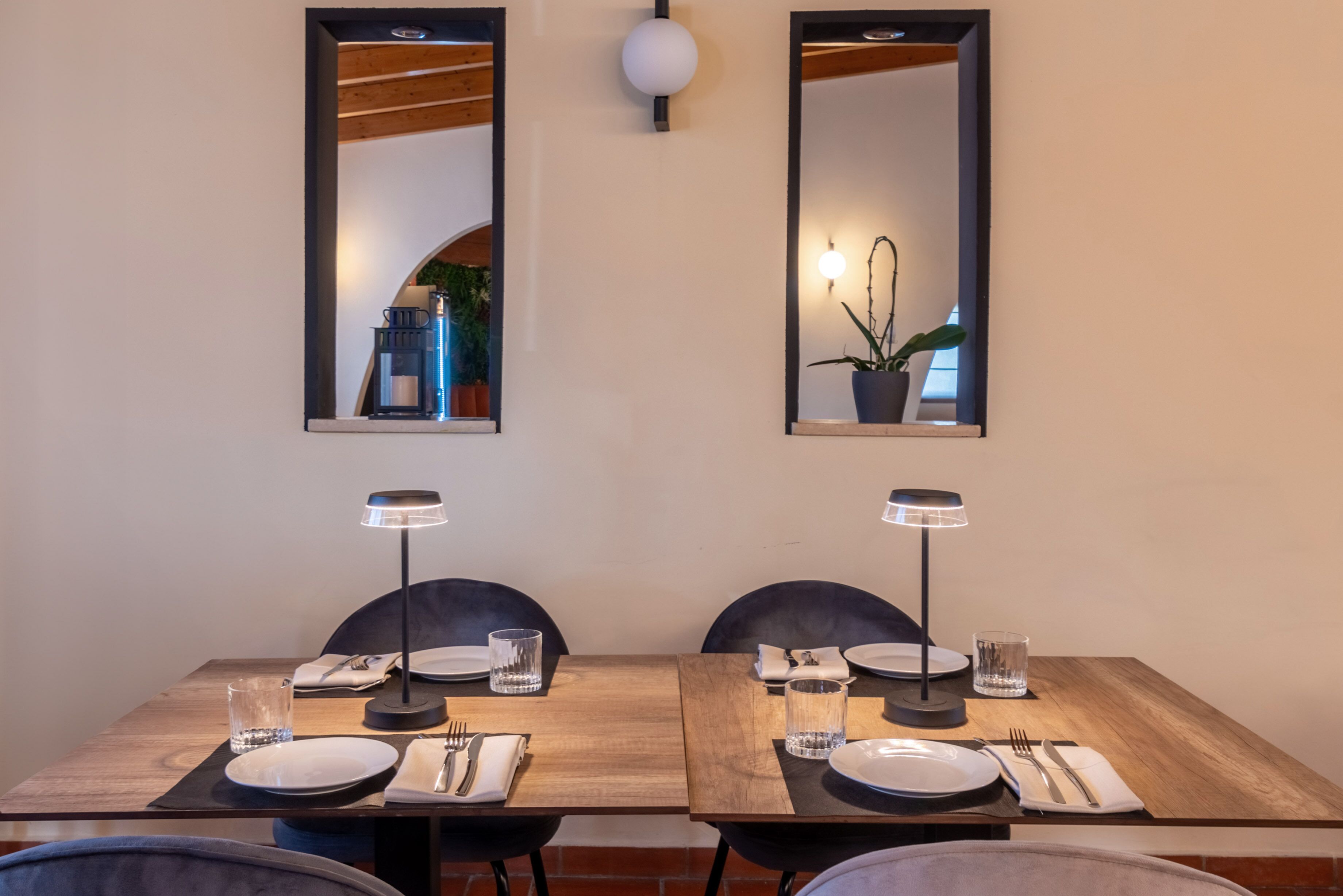 Comedor con una mesa de madera preparada para dos personas, dos sillas, dos lámparas de mesa y dos espejos montados en la pared.