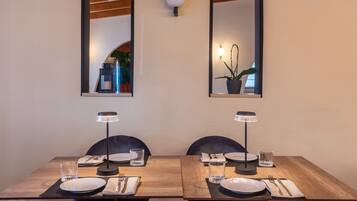 Comedor con una mesa de madera preparada para dos personas, dos sillas, dos lámparas de mesa y dos espejos montados en la pared.