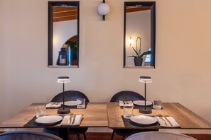 A dining area with a wooden table set for two, two chairs, two table lamps, and two wall-mounted mirrors. - Tiber Suite (Rome)