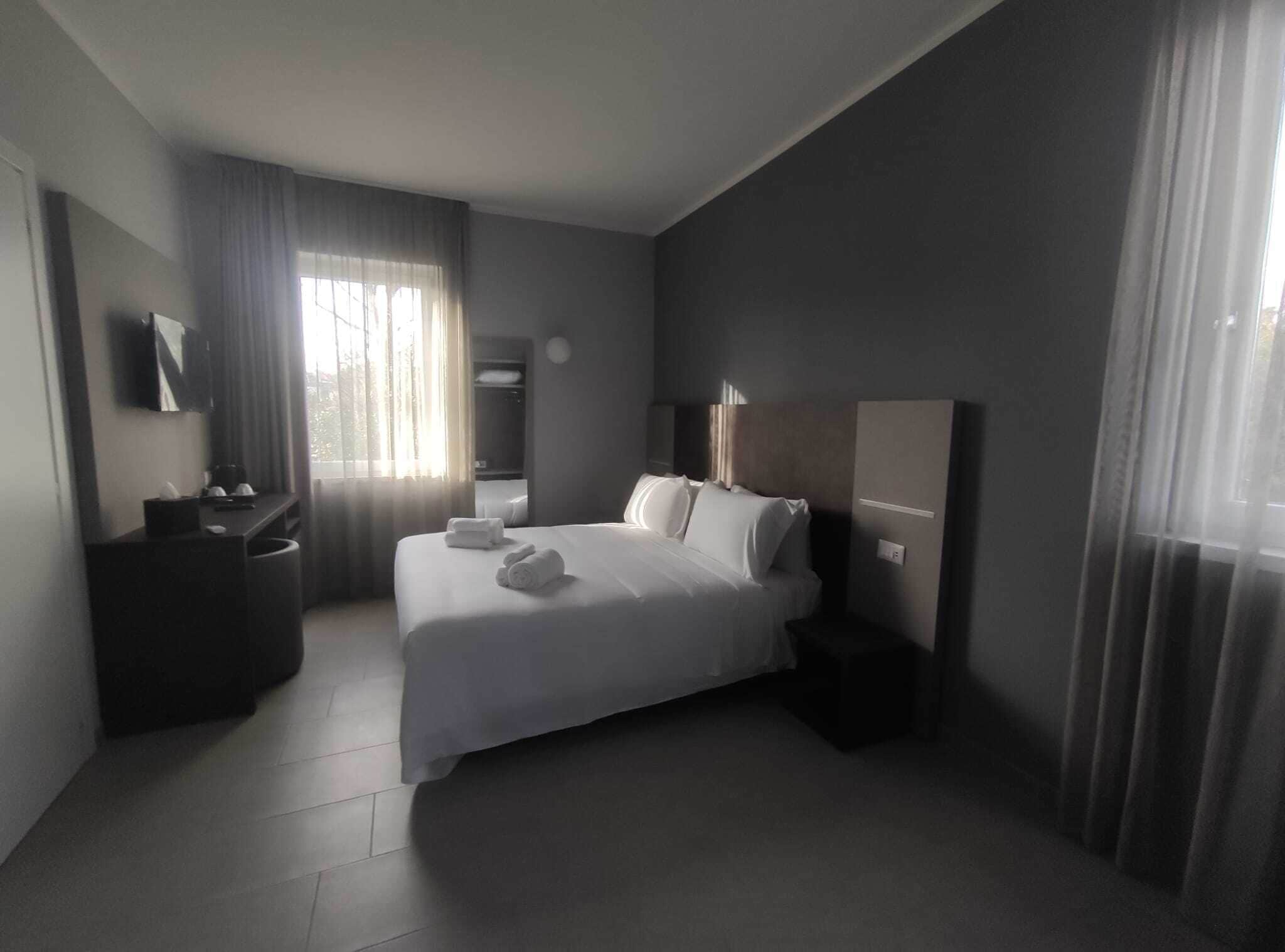 Een moderne hotelkamer met een opgemaakt bed, een nachtkastje, een kaptafel en een groot raam met gordijnen.