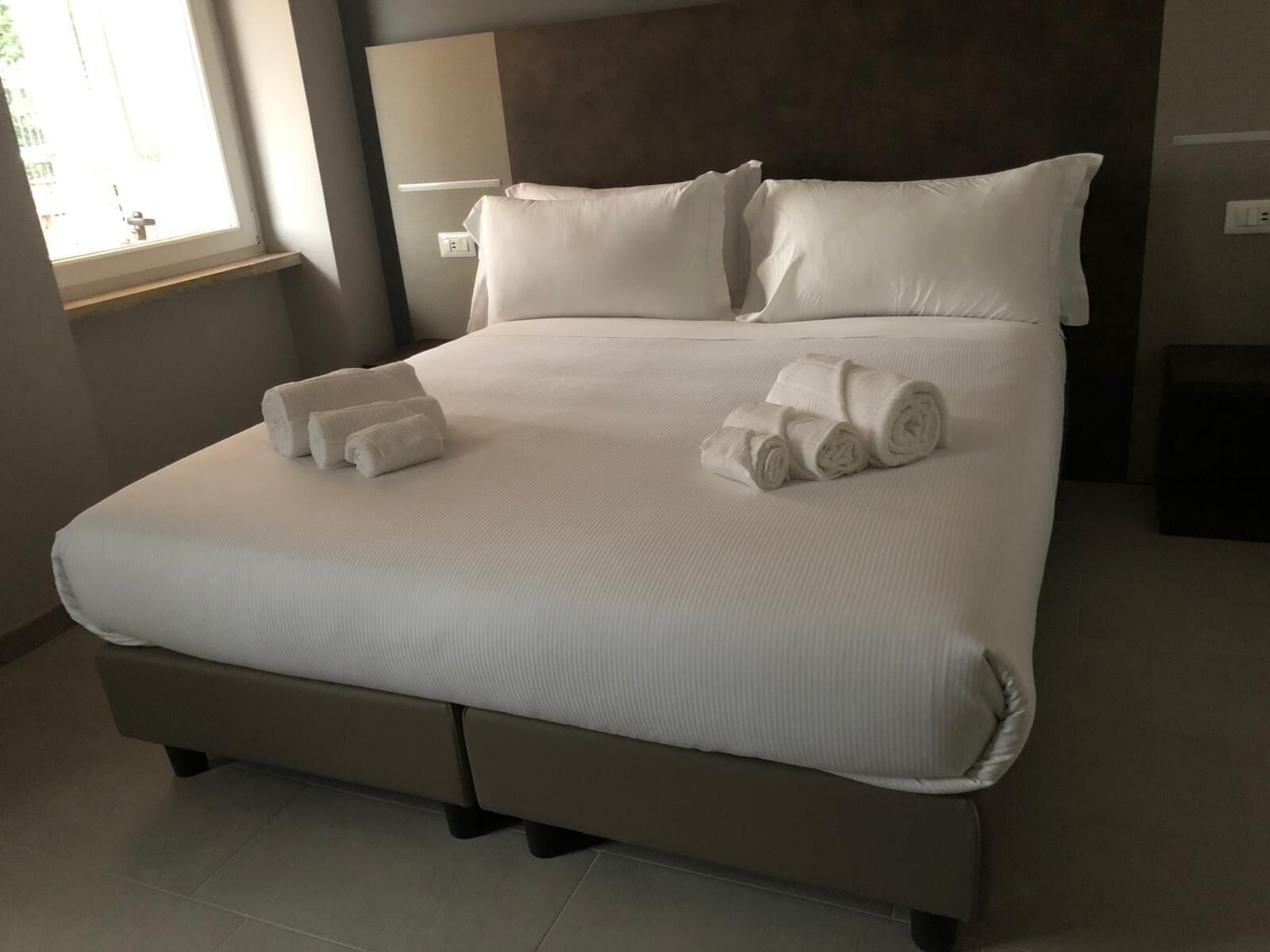 Un grand lit avec du linge de lit blanc et des serviettes pliées, une tête de lit et une table de chevet avec une lampe.