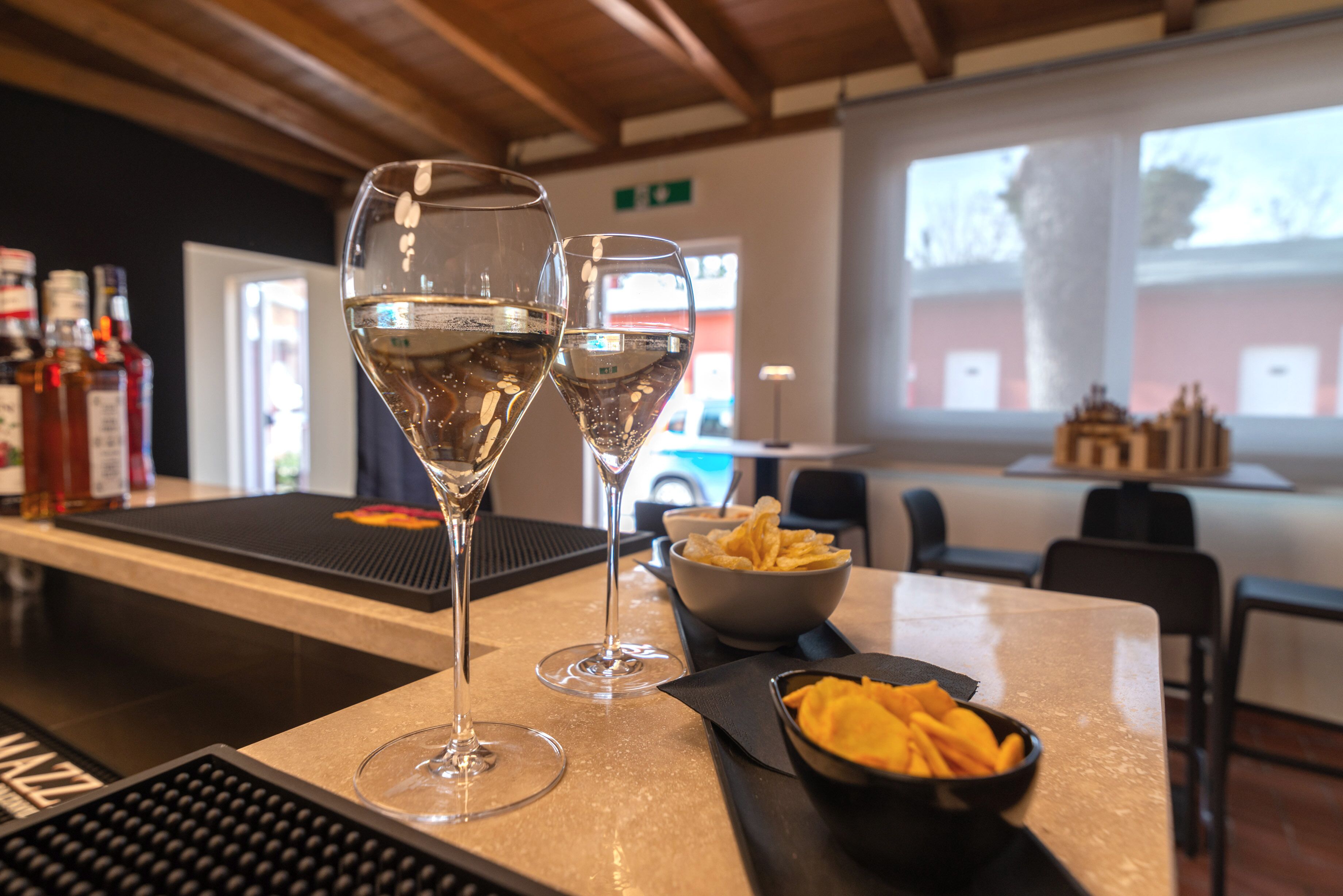 A bar area with two glasses of white wine, a bowl of chips, and a keyboard on the counter.