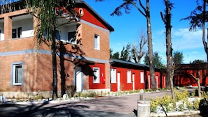 A multi-story building with red and brick exterior walls, a covered entrance, and a paved driveway. - Tiber Suite (Rome)