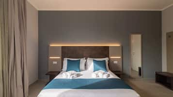 A modern hotel room with a large bed, two bedside tables, a nightstand, a mirror, and a curtain.
