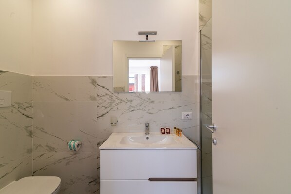 A bathroom with a marble wall, a white sink with a mirror above it, and a toilet.