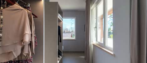Um corredor com um cabideiro, uma janela e uma porta que dá para outro quarto.