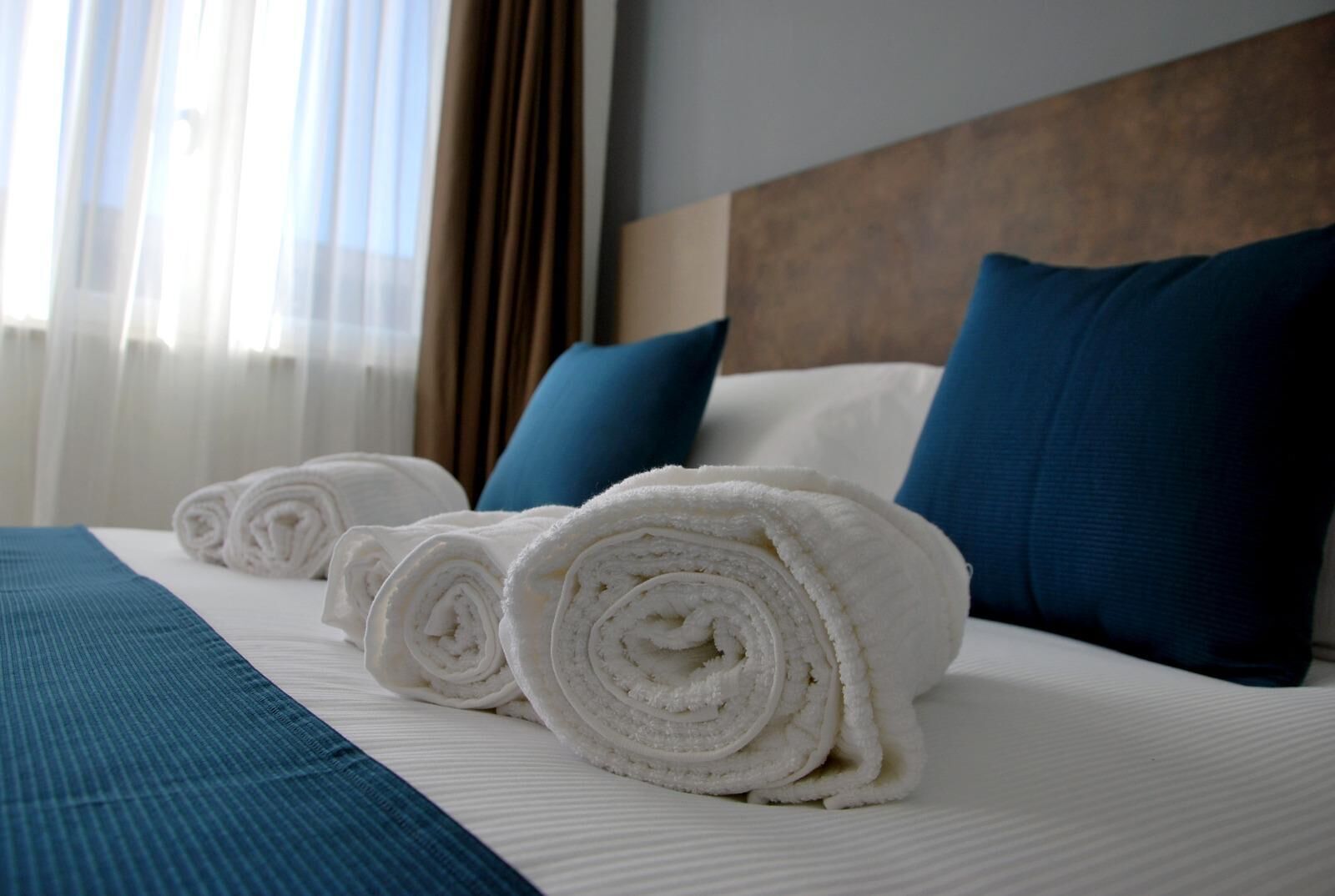 Un letto rifatto con asciugamani bianchi arrotolati, cuscini blu e copripiumone blu in una camera d'albergo.