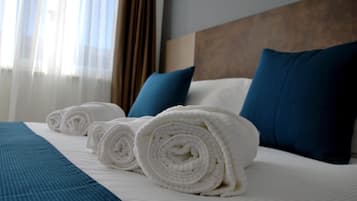 Un letto rifatto con asciugamani bianchi arrotolati, cuscini blu e copripiumone blu in una camera d'albergo.