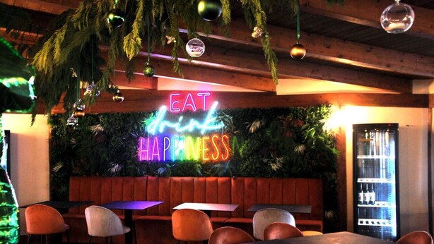 A restaurant interior with a neon sign reading "EAT drink HAPPINESS" and a seating area with tables and chairs. - Tiber Suite (Rome)
