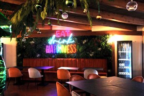 A restaurant interior with a neon sign reading "EAT drink HAPPINESS" and a seating area with tables and chairs. - Tiber Suite (Rome)
