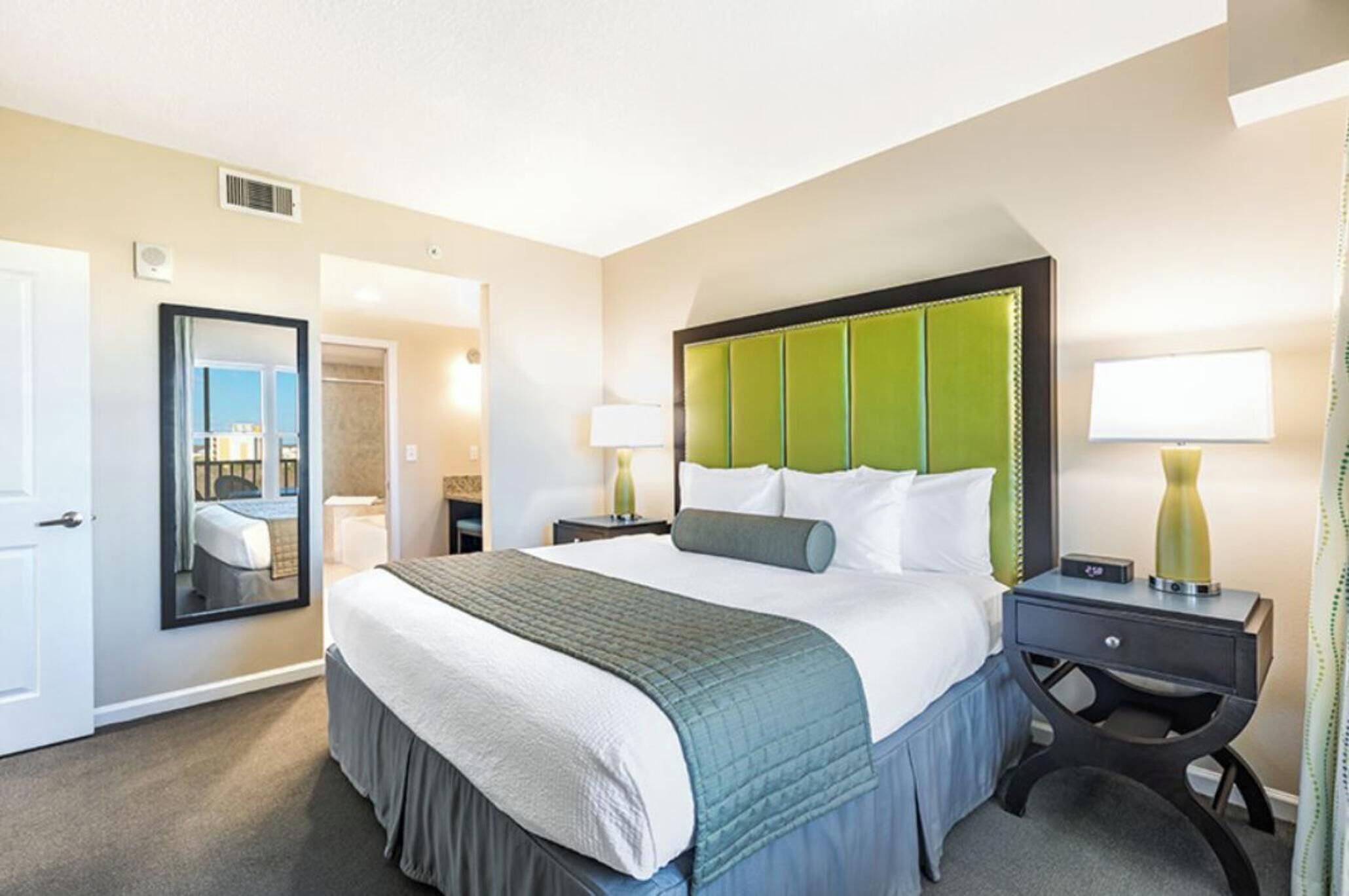 Une chambre d’hôtel avec un lit, des tables de chevet, un miroir et une porte.