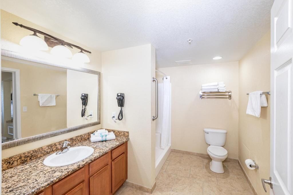 A bathroom with a sink, mirror, towel rack, shower, and toilet.