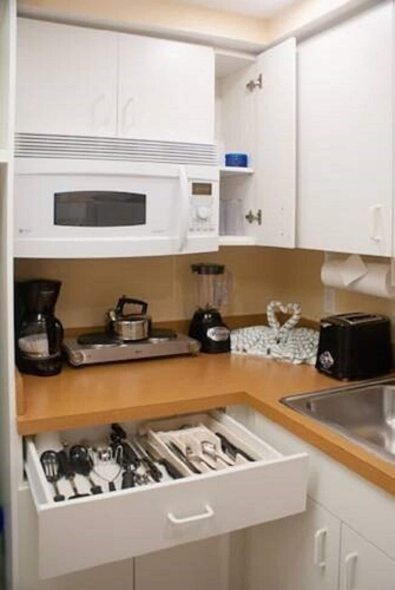 Cozinha compacta com micro-ondas, cafeteira, torradeira e gaveta com utensílios.