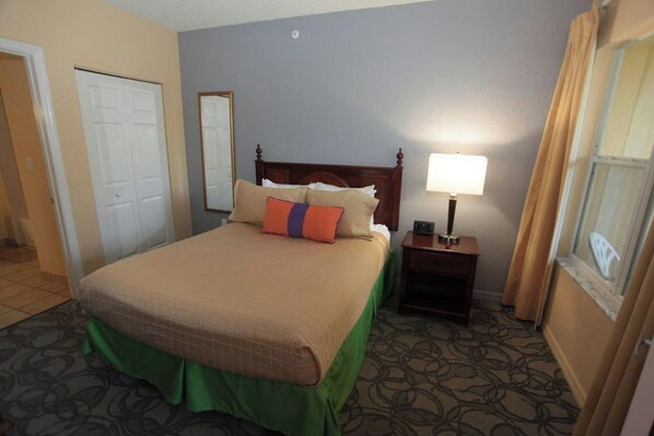 A hotel room with a bed, a bedside table with a lamp, a mirror, and a door. - Vacation Village at Parkway (Kissimmee)