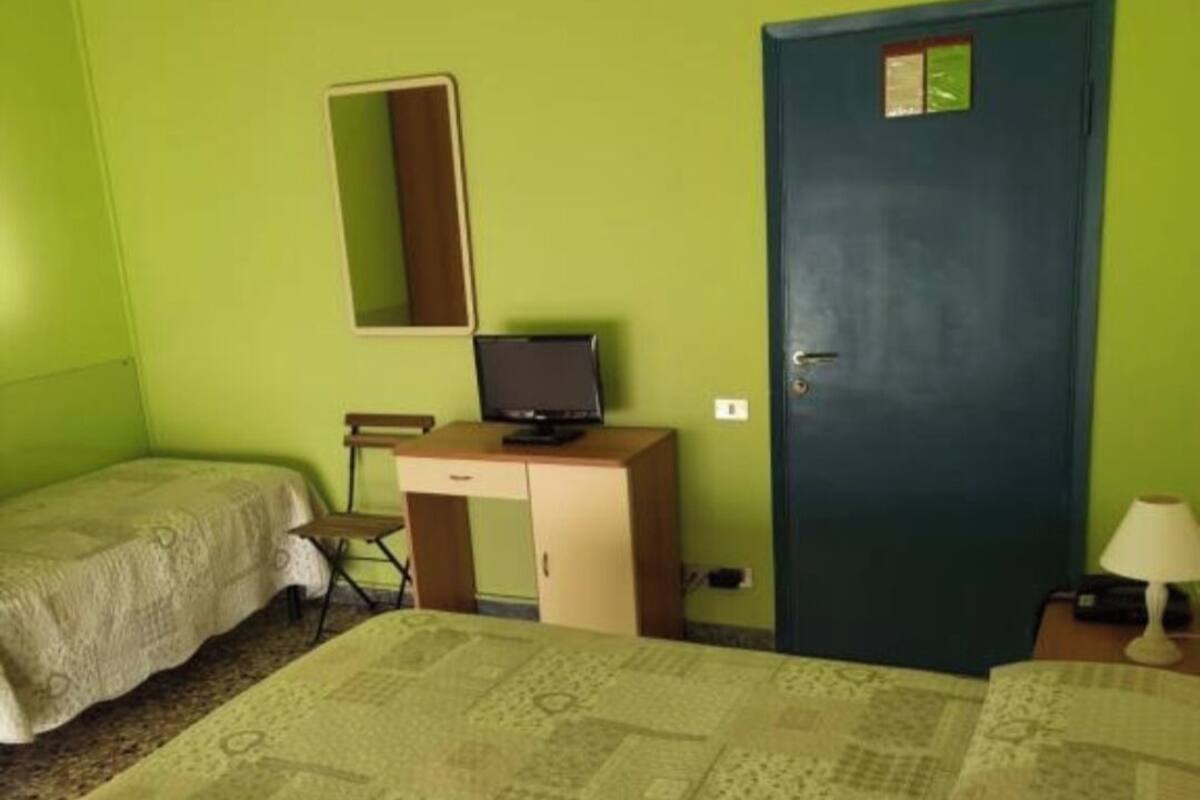 Ein Zimmer mit zwei Betten, einem Schreibtisch mit Computer, einer Tür und einem Spiegel an der Wand.
