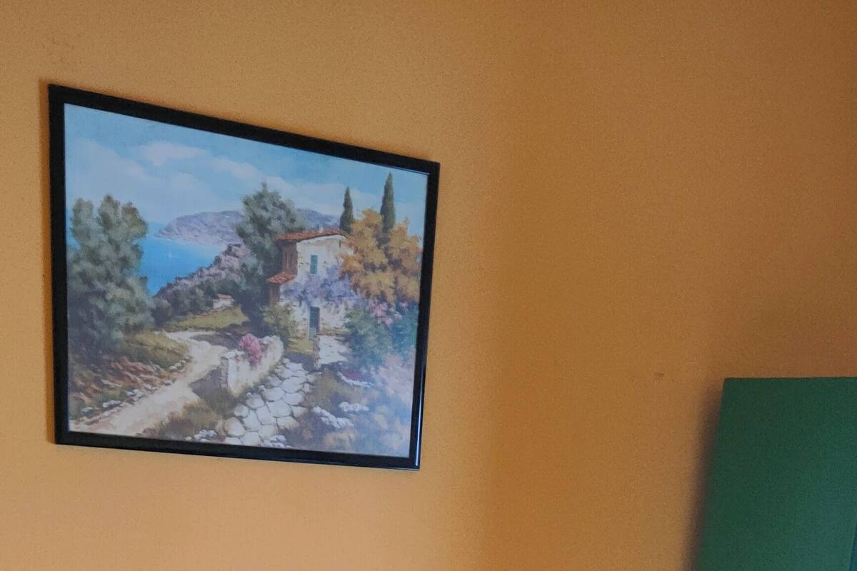 Ein Bett mit einer türkisfarbenen Bettdecke, einem weißen Kopfkissen und einem Landschaftsbild an der Wand.