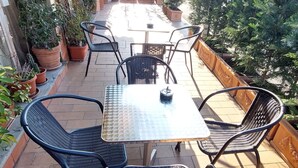 An outdoor patio with a table and chairs, surrounded by potted plants and a yellow awning.