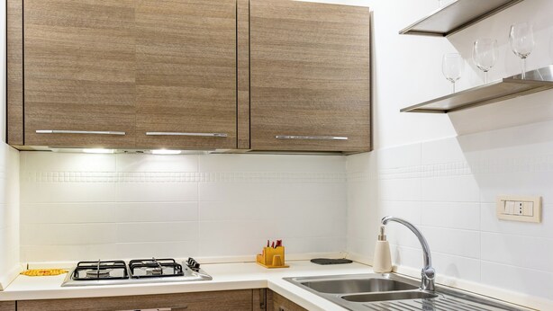Eine moderne Küche mit Holzausbau, einer weißen Arbeitsplatte, einem Gasherd und einer Spüle aus Edelstahl.