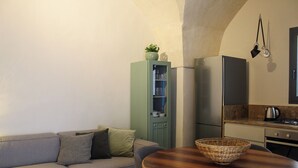 Un espacio habitable compacto con sofá, un mueble bajo con puertas de vidrio, una zona de cocina con hervidor y un colgador de techo.