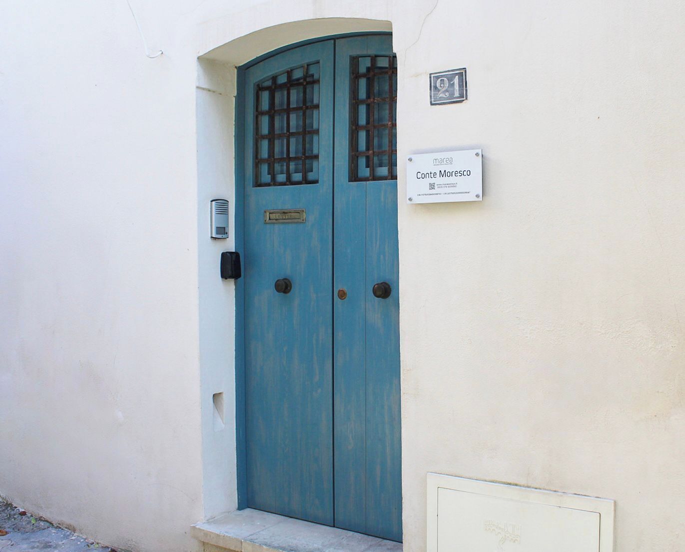 Una porta blu con un motivo a griglia, una cassetta postale e un cartello con su scritto "Conte Moresco".