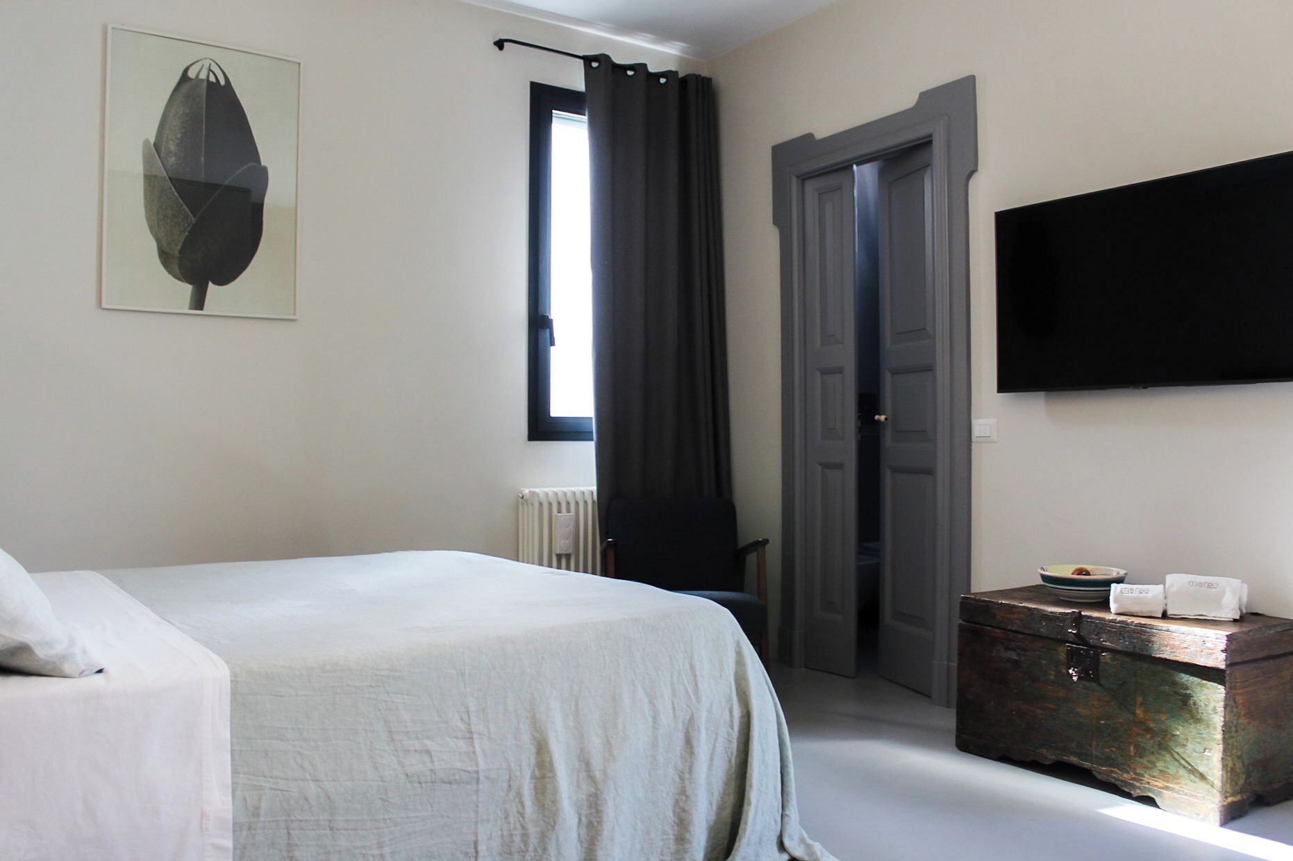 Ein Hotelzimmer mit Bett, Kommode, Fernseher und einem Fenster mit Vorhängen.