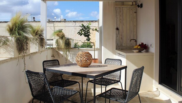 Un patio al aire libre con una mesa, sillas, una cesta de mimbre y plantas en macetas.