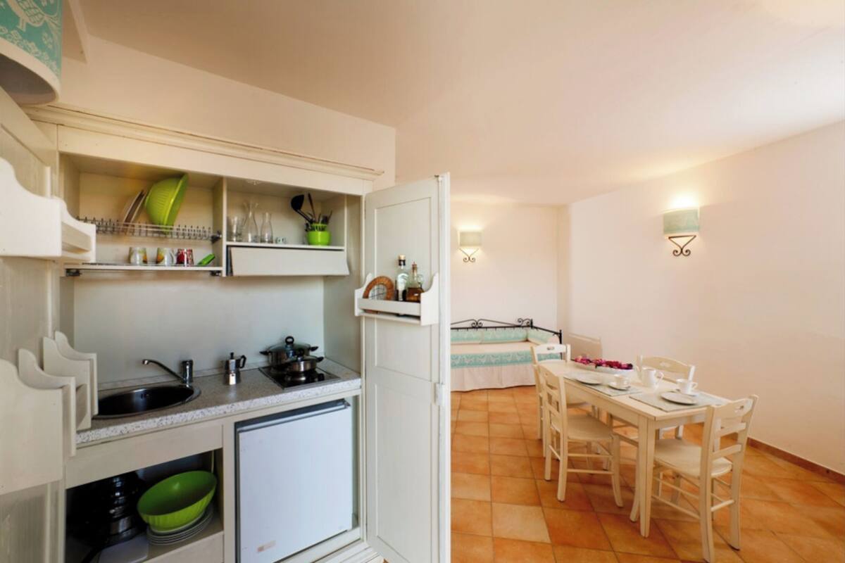 Una cocina compacta con pileta, cocina y estanterías, y un comedor con mesa y sillas.