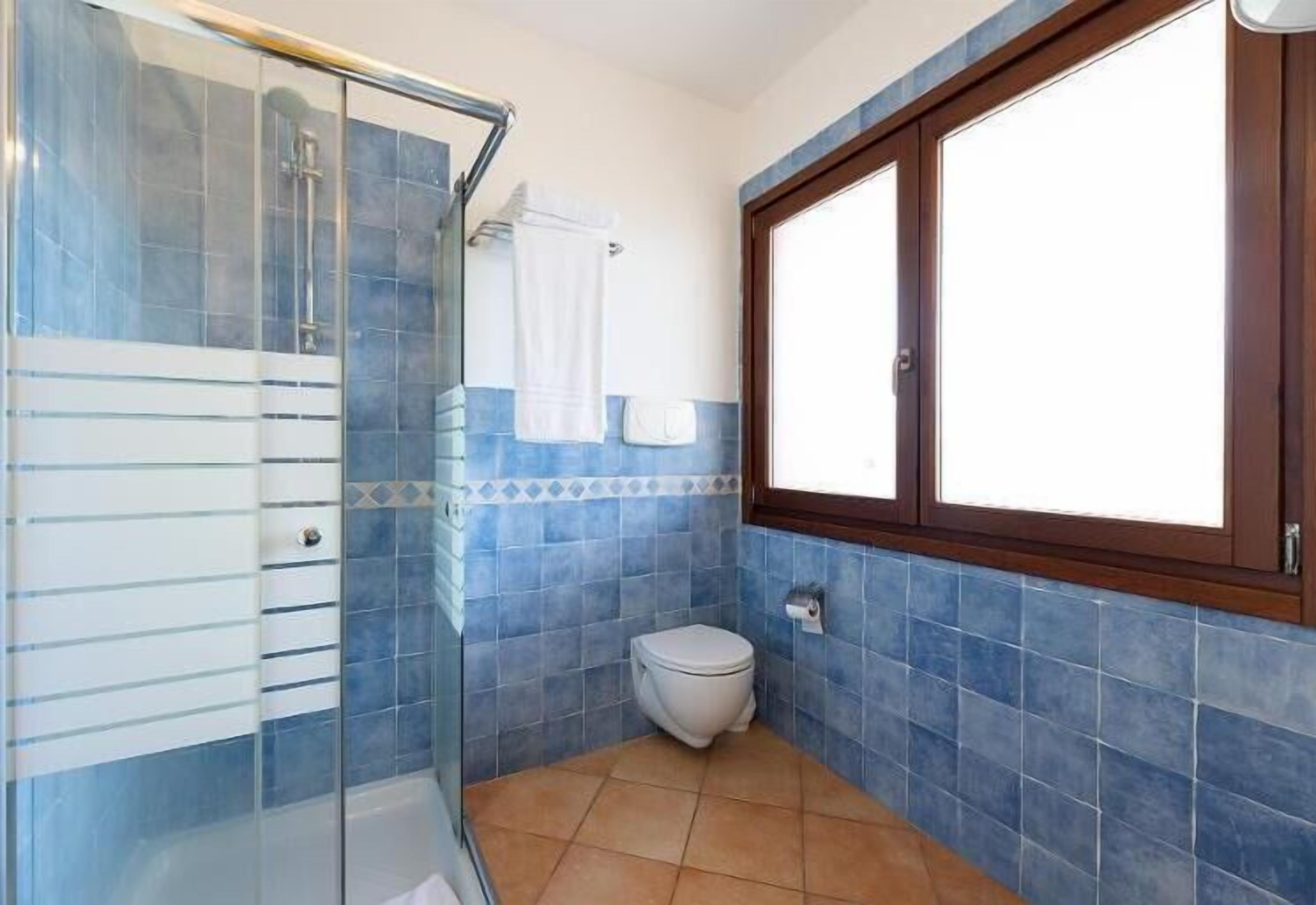Et badeværelse med glasbrusekabine, toilet og et vindue.