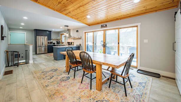 A spacious kitchen with wooden ceiling, a dining area with a large table and chairs, and a view through large windows.