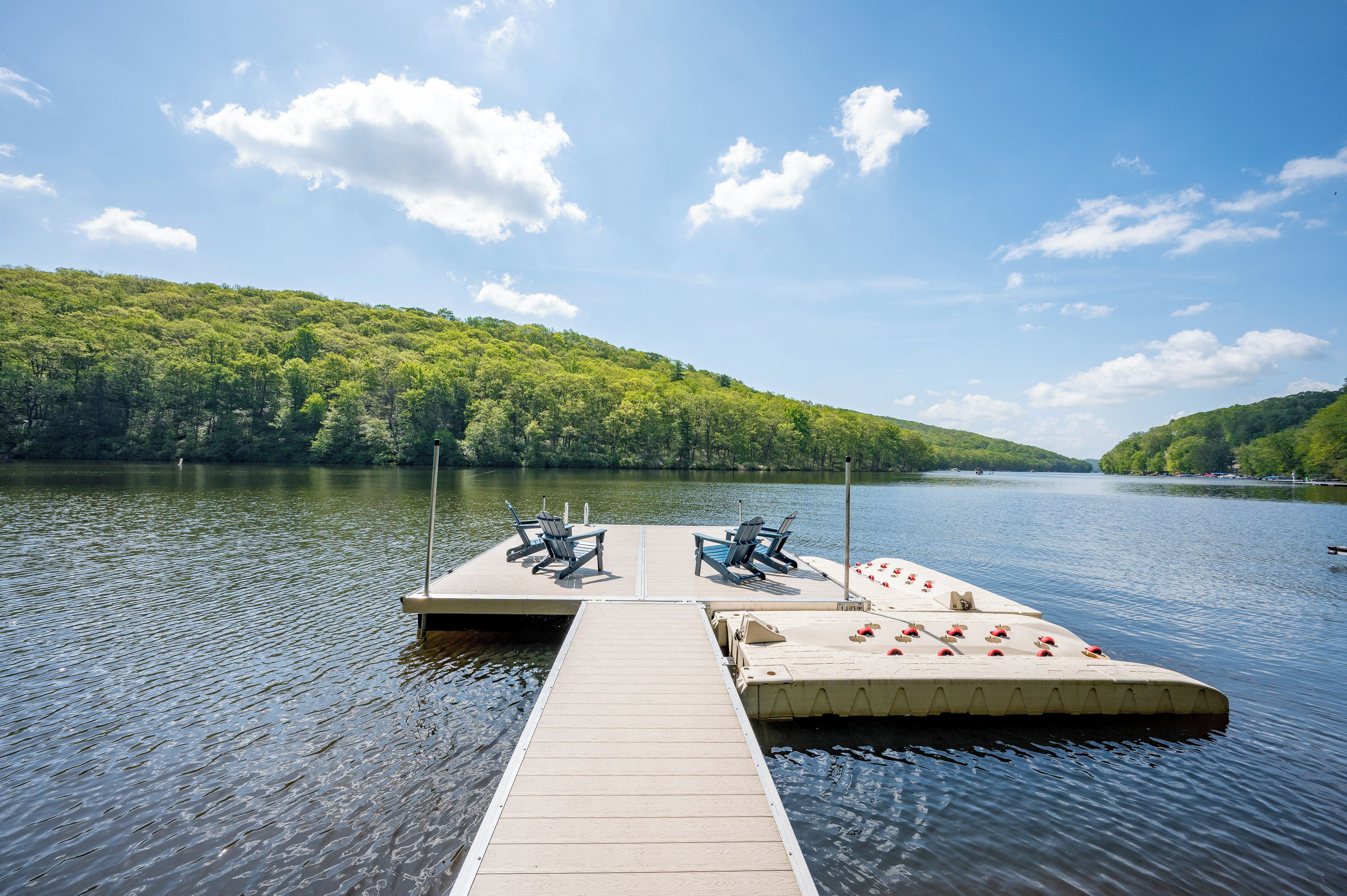 A wooden dock extending into a calm lake, with two chairs and a small table on the dock.
