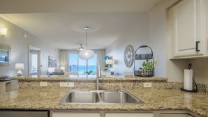 A kitchen with granite countertops, stainless steel sink, white cabinets, and a view of the city through large windows.