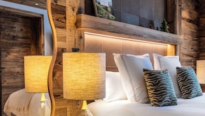 A bedroom with a wooden ceiling, a large mirror, a bed with white linens, and two lamps. - Silverstone by Alpine Resorts (Val-d'Isere)