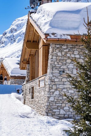 A stone building with wooden balconies, snow-covered roofs, and a mountainous backdrop. - Silverstone by Alpine Resorts (Val-d'Isere)