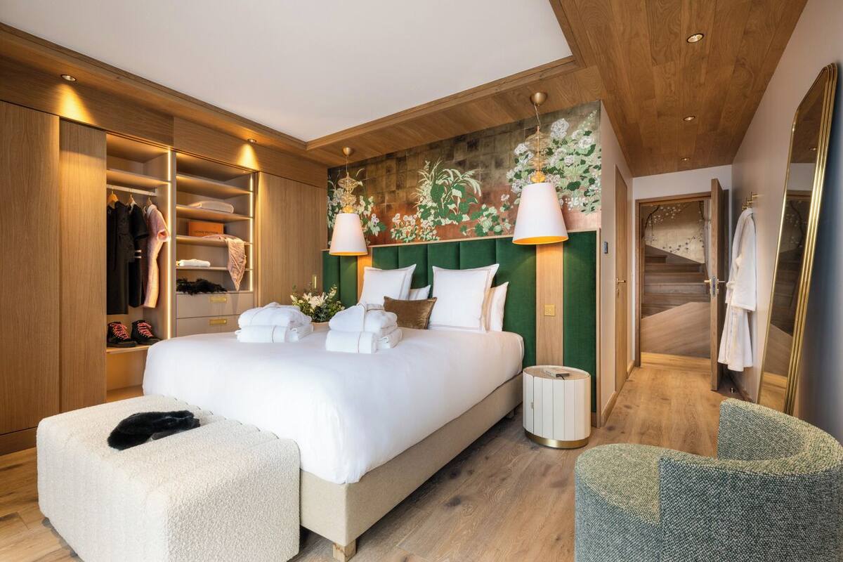 A modern hotel room with a large bed, a walk-in closet, a green headboard, and a staircase leading to another level.